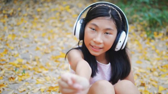 亚洲女孩使用耳机，坐在户外的黄叶上，玩烟火，生活方式概念。