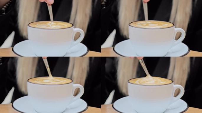 一个不被认可的白人金发女人用一小勺在一杯陶瓷杯卡布奇诺咖啡中搅拌糖