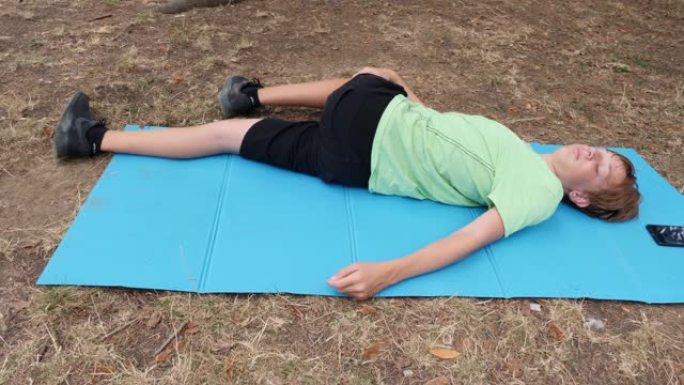 十几岁的男孩躺在公园的垫子上-慢动作