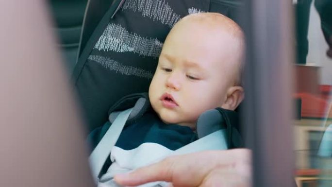 特写男婴坐在车内的婴儿汽车座椅上。父亲的手系安全带。透过打开的门拍照。慢动作