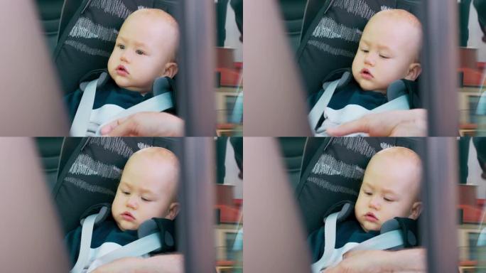 特写男婴坐在车内的婴儿汽车座椅上。父亲的手系安全带。透过打开的门拍照。慢动作