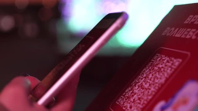 用智能手机扫描二维码。女人在夜间霓虹灯背景上使用智能手机上的应用程序读取条形码