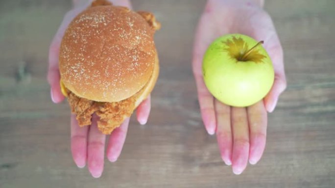 在卡路里汉堡和青苹果之间进行选择。妇女手握有害健康食品