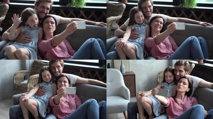 幸福的三口之家坐在沙发上，微笑的母亲拿着手机，自拍。兴奋的夫妇与女儿合影或与祖父母在线通话。