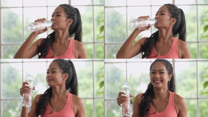 亚洲妇女在家完成瑜伽运动后喝一瓶水