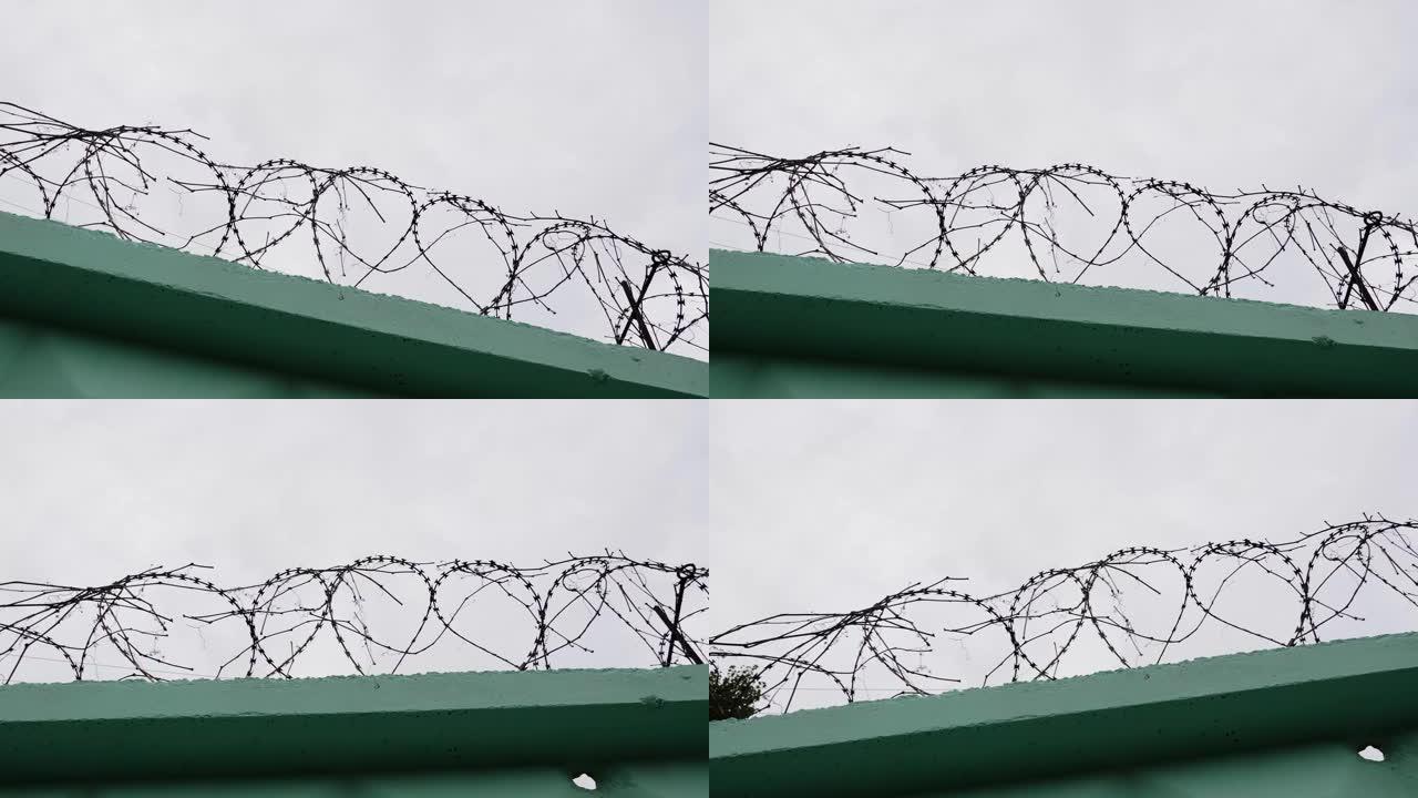 监狱里的铁丝网。带倒钩的监狱铁丝网。绿色围栏，铁丝网对着灰色的天空。