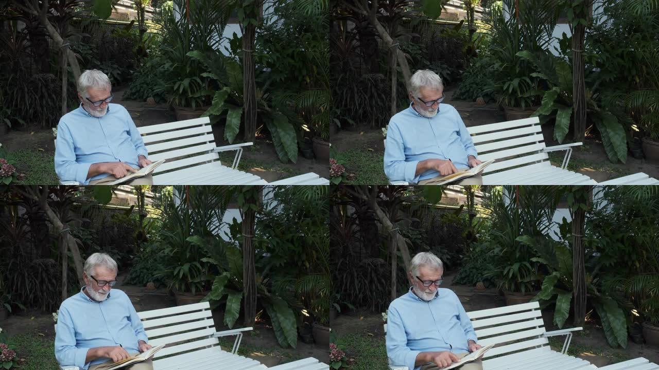 祖父或老人看书独自坐在花园里的长凳上