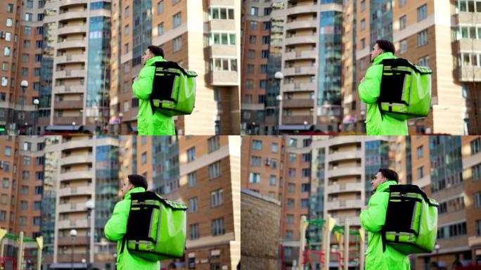 穿着绿色制服的年轻送货员的中等跟踪镜头，带着保暖背包走在城市街道上运送食物