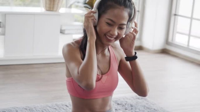 穿着运动服的美丽亚洲女性在家里的客厅里做瑜伽锻炼时听音乐。