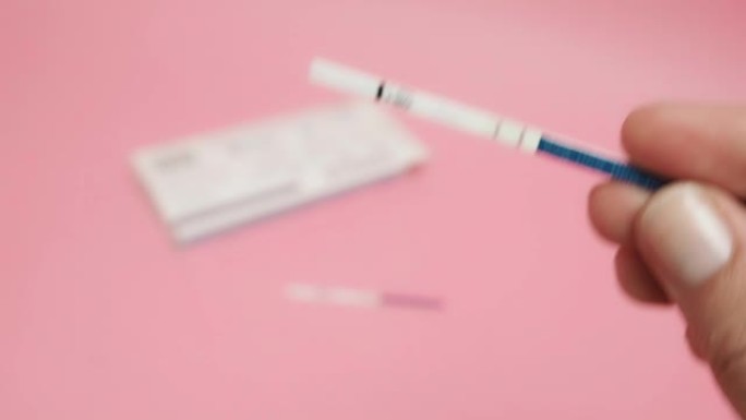 女性手握阳性妊娠试验孤立在粉红色背景。蓝色条上的缩写HCG表示人绒毛膜促性腺激素是一种由细胞产生的激