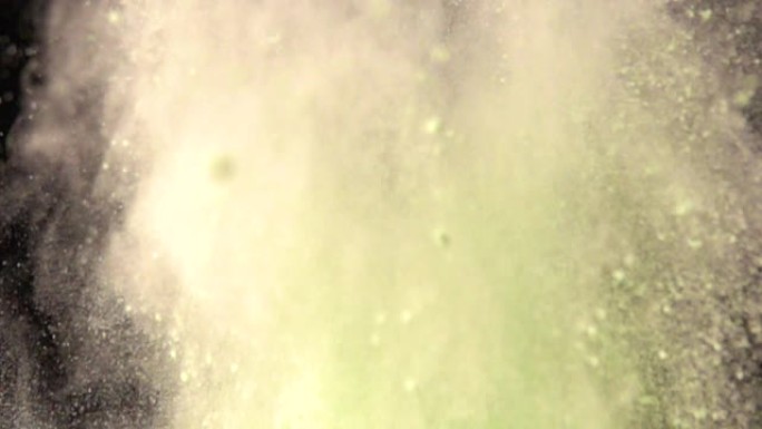超慢动作爆炸彩色绿色粉末在黑暗孤立的背景。粉末团向上飞，与烟雾混合。