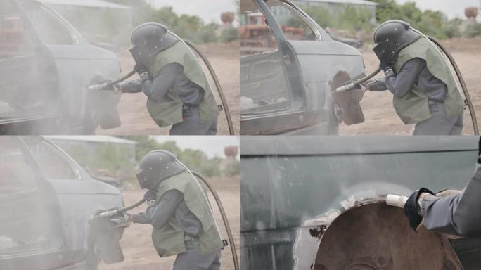 一个穿着防护服和安全帽的人用沙流加工金属。穿着喷砂制服的工人