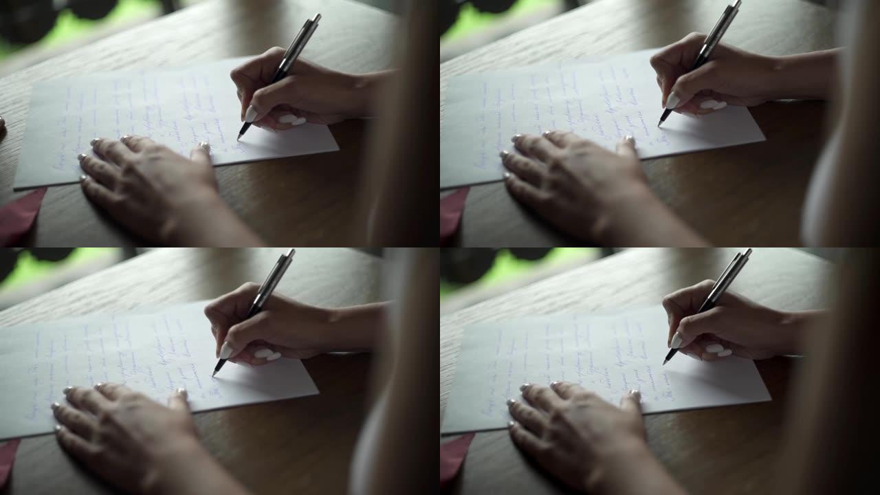 年轻女子用笔在白纸上写给她心爱的新郎的情书，坐在阳台附近房间的桌子旁。阳台外的绿草。婚礼准备。新娘的