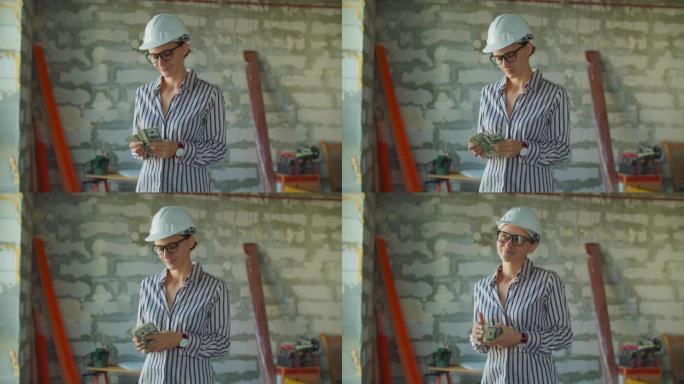 年轻微笑的女工戴着白色安全帽数钱，站在建筑工地。工头持有现金用于房屋装修过程。“热固性粉末混合” 盒