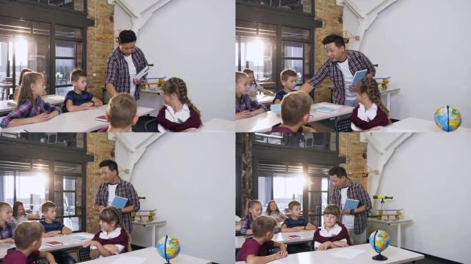 年轻的韩国老师走在课桌之间，将教科书放在课桌上，而白人学生则坐在课桌旁