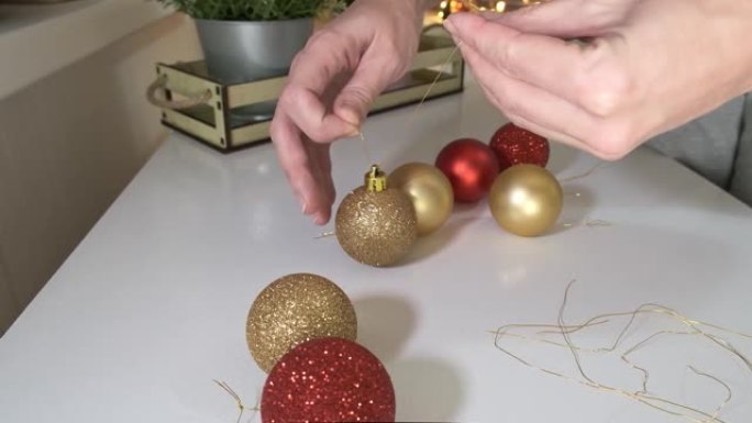女人双手准备庆祝新年和圣诞节，她用绳子提供装饰性的彩色球，以便将其挂在杉木松树上。背景上有花环的特写