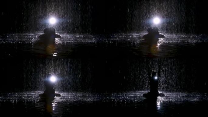黑色剪影女人在雨中进行瑜伽练习。Studio light在水面上产生微光。慢动作