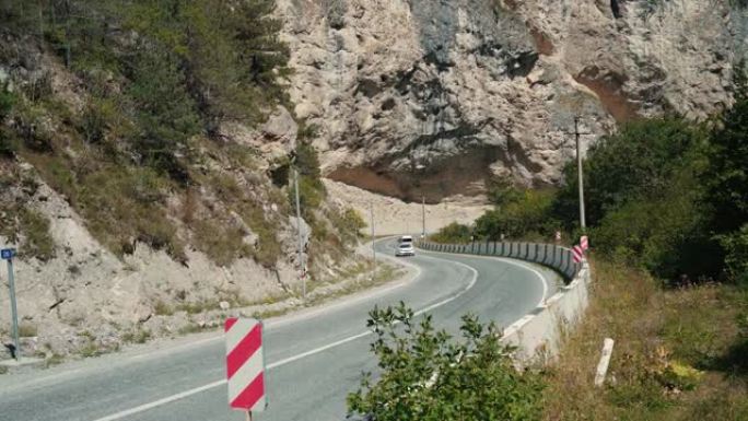 山区有交通标志的弯曲道路。红色对角线保持左障碍物交通标志放置在弯曲的柏油路穿过山区的石头边界上
