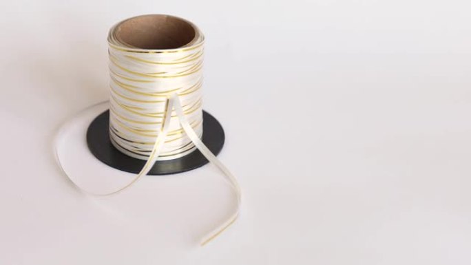 薄的金色和白色包装胶带，用于在白色孤立的背景上成卷的礼物。包装礼品的丝带。