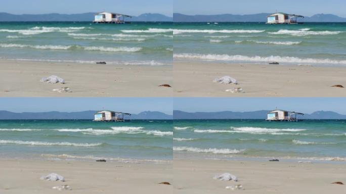 海浪在海滩上掠过，可以看到蓝色的大海，岛屿和漂浮的小屋。