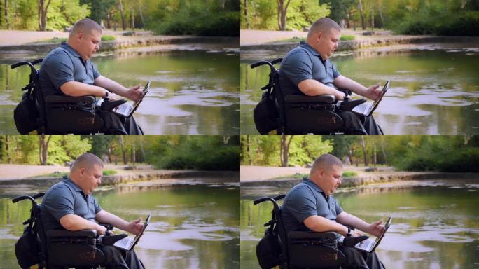 轮椅男子。残疾人。年轻的残疾人，坐在自动轮椅上，在秋天的晴天，在湖边的城市公园里，在笔记本电脑上工作