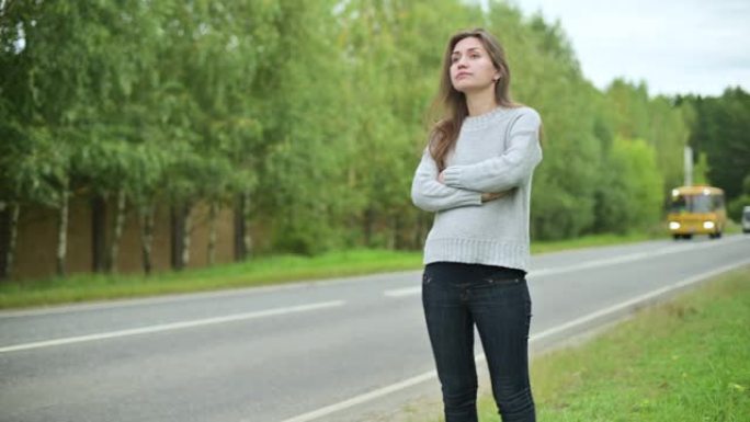 相机放大了一个在路上等待乘车或公共汽车的女人