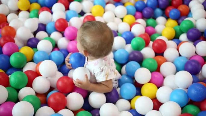 一岁的婴儿在操场上。在一个特殊的游泳池里玩五颜六色的塑料球。侧视图