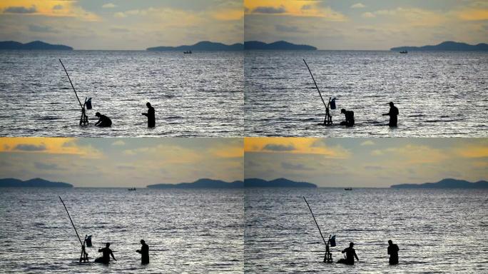 剪影两名男子在海上收集网将鱼分开并存放在桶中