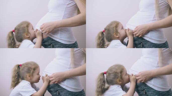 可爱的小女孩在灯光室亲吻怀孕的妈妈肚子
