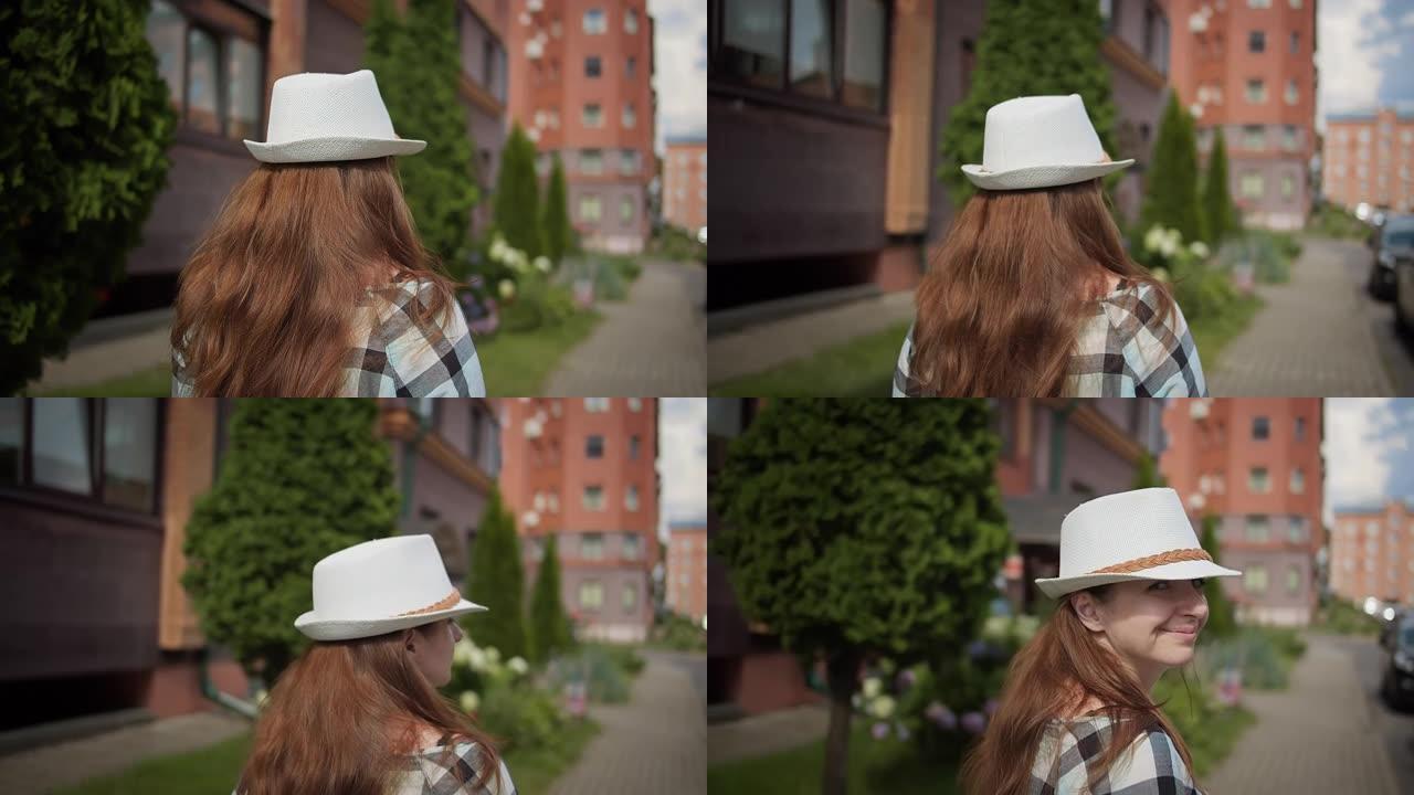 戴着帽子的女旅行者走在城市的街道上，向后看，转身看着相机