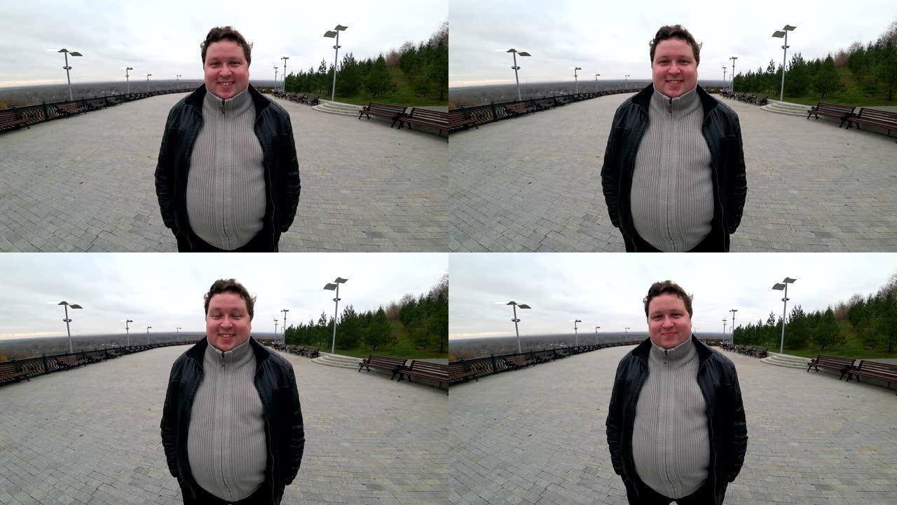 广角镜: 年轻的胖子站在城市景观中，看着相机并微笑着