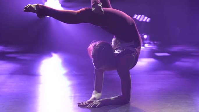 一位女孩艺术体操运动员表演倒立和平衡。女运动员在紫色背景的封闭工作室里训练。剪影。为比赛做准备。特写