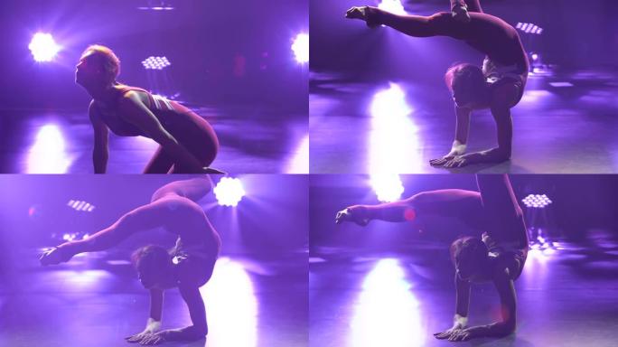 一位女孩艺术体操运动员表演倒立和平衡。女运动员在紫色背景的封闭工作室里训练。剪影。为比赛做准备。特写