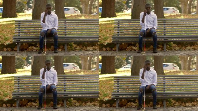 盲人黑人年轻人坐在公园的长凳上。失明，自治