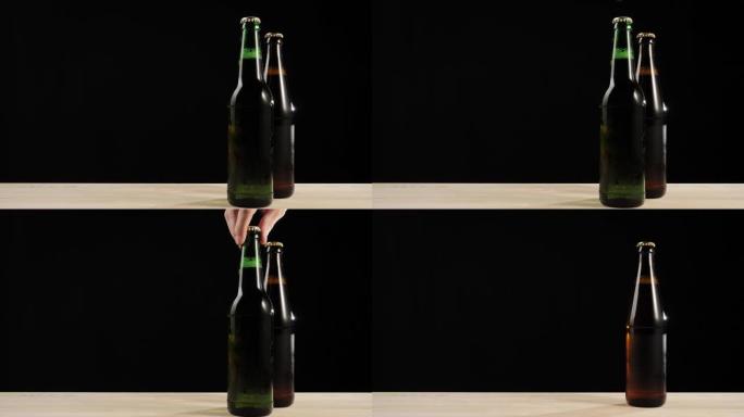 新鲜啤酒。手从黑色背景下的木制桌子上拿了一个绿色的瓶子，里面有美味的工艺啤酒，靠近棕色瓶子。水滴冷新