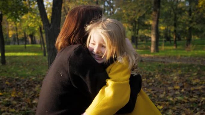 迷人的小女孩很少在秋天的公园里落叶中在新鲜空气中放松时遇到她心爱的母亲的怀抱