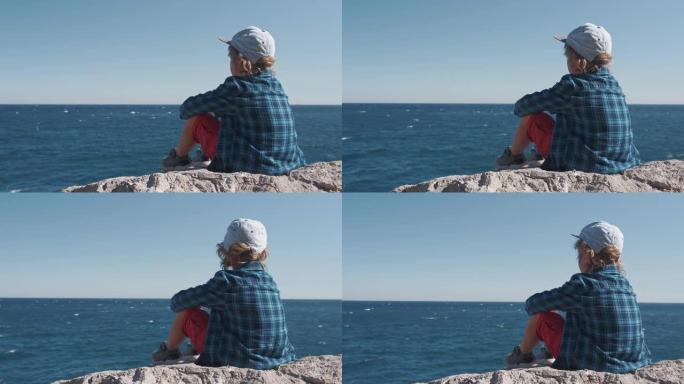 孩子坐在山顶上，看着海浪。