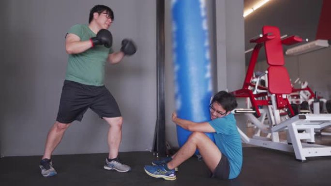 亚洲胖子用沙袋练习拳击，而他的朋友拿着沙袋