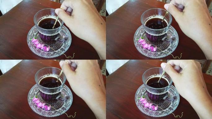 木制桌子上的玻璃杯里的咖啡。用手在木桌上的杯子里搅拌咖啡