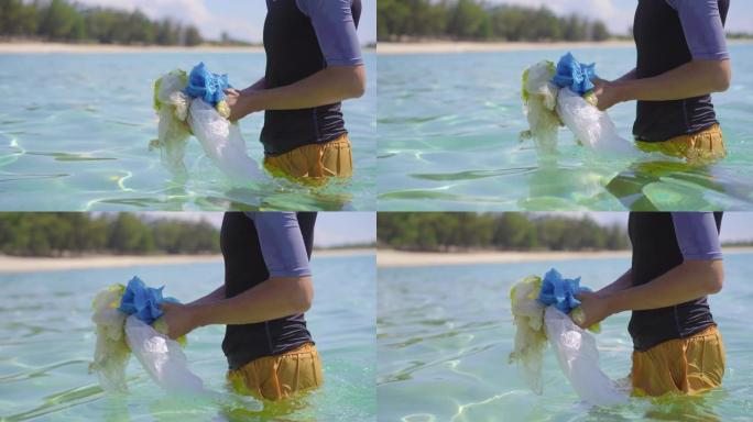 在美丽的绿松石海中收集塑料袋的男子的手持照片。天堂海滩污染。人为污染造成的沙滩上的垃圾问题。清洁环境