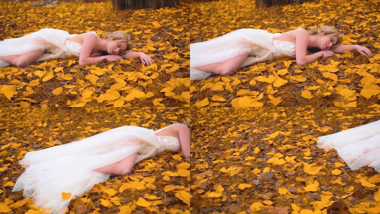 穿着白色婚纱的金发女孩躺在秋天的黄叶上