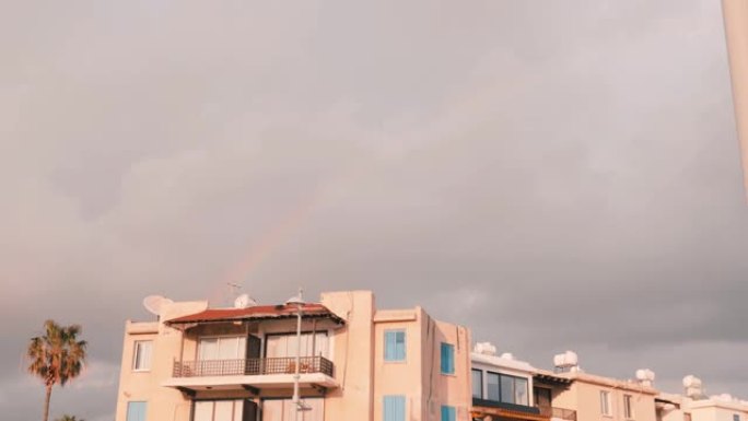 天空中的彩虹。雨后彩虹。暴风雨后彩虹的出现。恶劣天气下灰色多云的天空。前面有建筑的彩色曲线