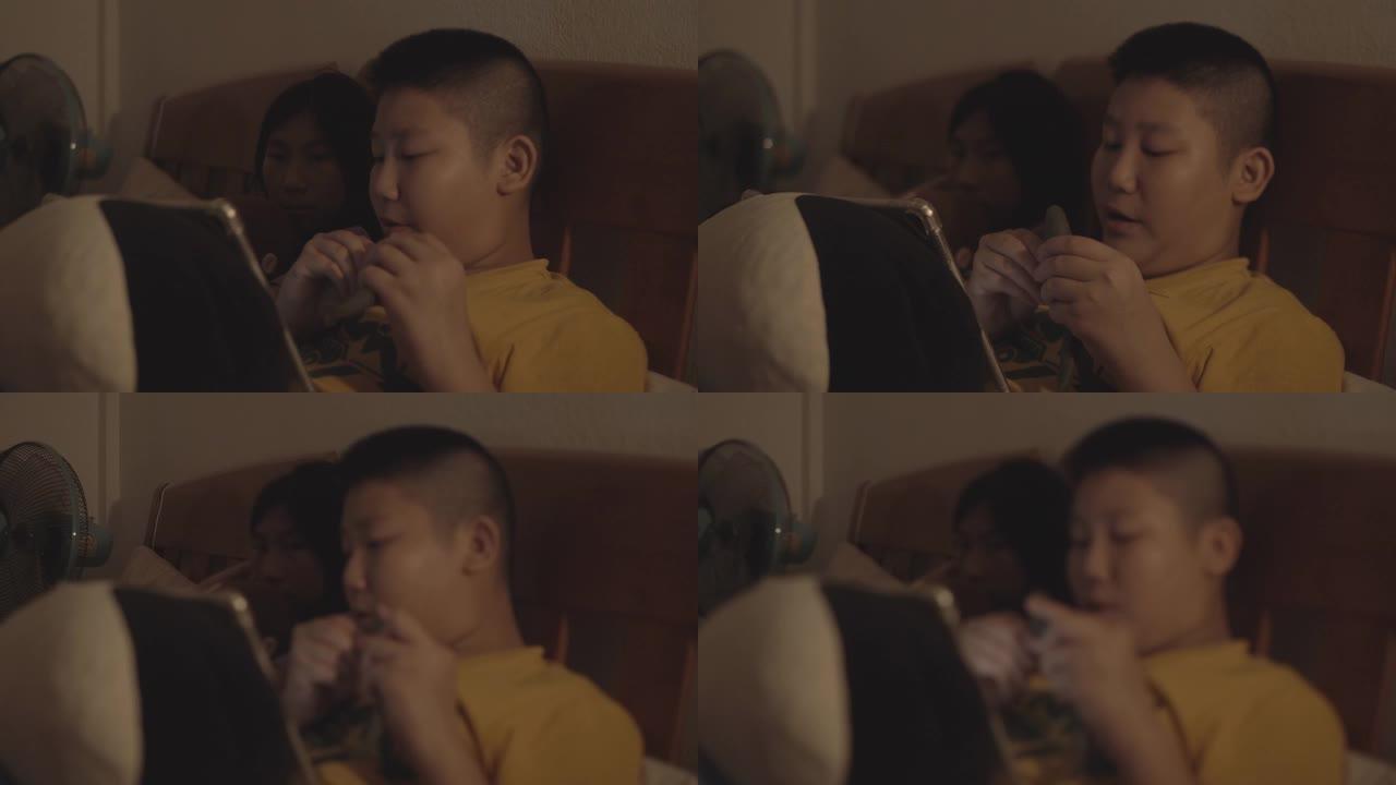 亚洲男孩和女孩晚上一起在床上用数字平板电脑看电影。