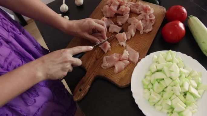年轻女子的手在厨房的木制砧板上切鸡肉的特写