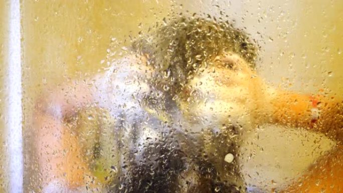 一个不认识的女人在洗澡。年轻女孩站在淋浴间享受着温暖的水。有魅力的女士照顾自己洗头。美丽的风景在玻璃