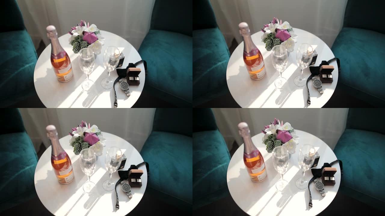 香槟，带两个香槟长笛，手表，袖扣，领结和插花在窗户附近沙发椅之间的白色圆桌上