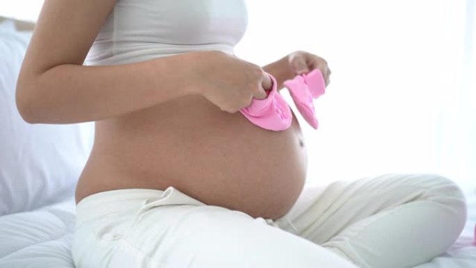 怀孕快乐的女人手里拿着粉红色的婴儿鞋