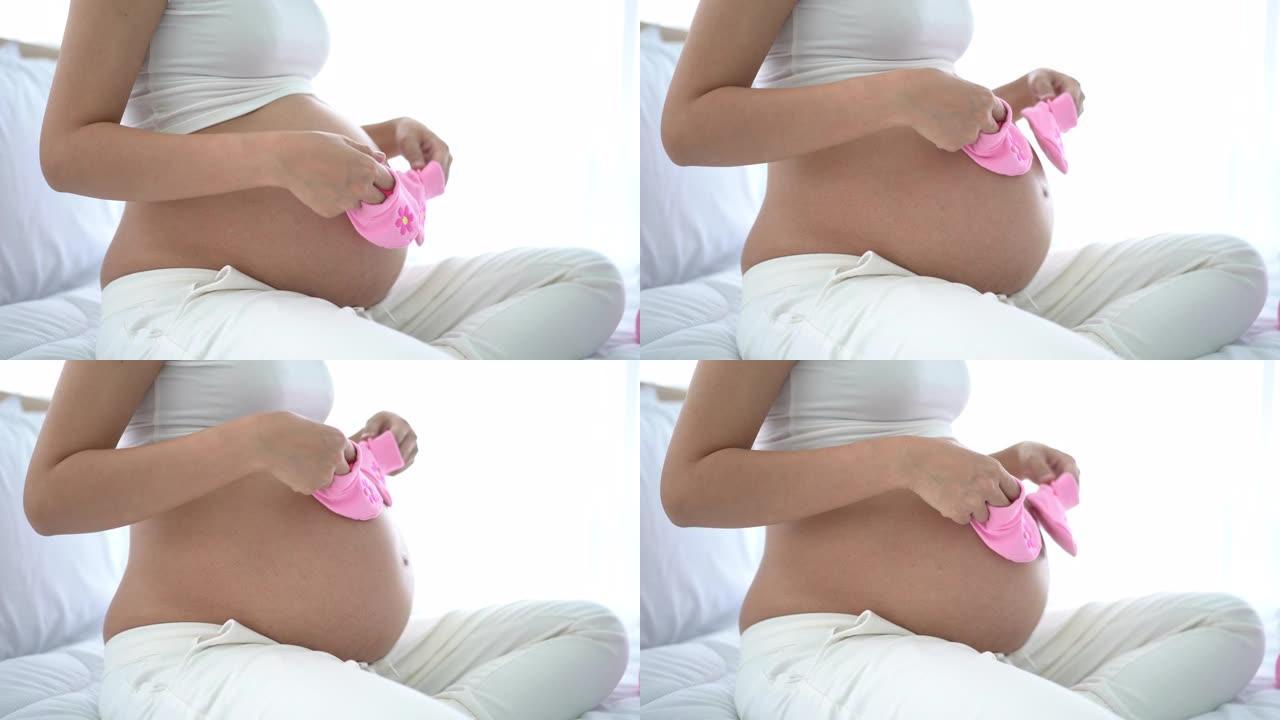 怀孕快乐的女人手里拿着粉红色的婴儿鞋