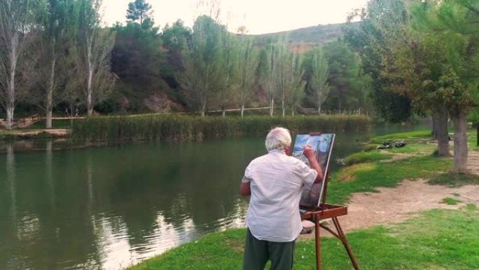 一位年老的艺术家在河岸上画一幅油画