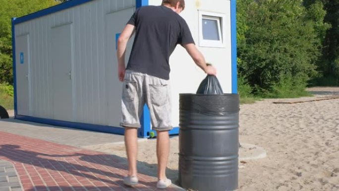 一名男性志愿者将垃圾袋扔进城市海滩岸边的容器中。清洁，秩序，生态。环保理念。